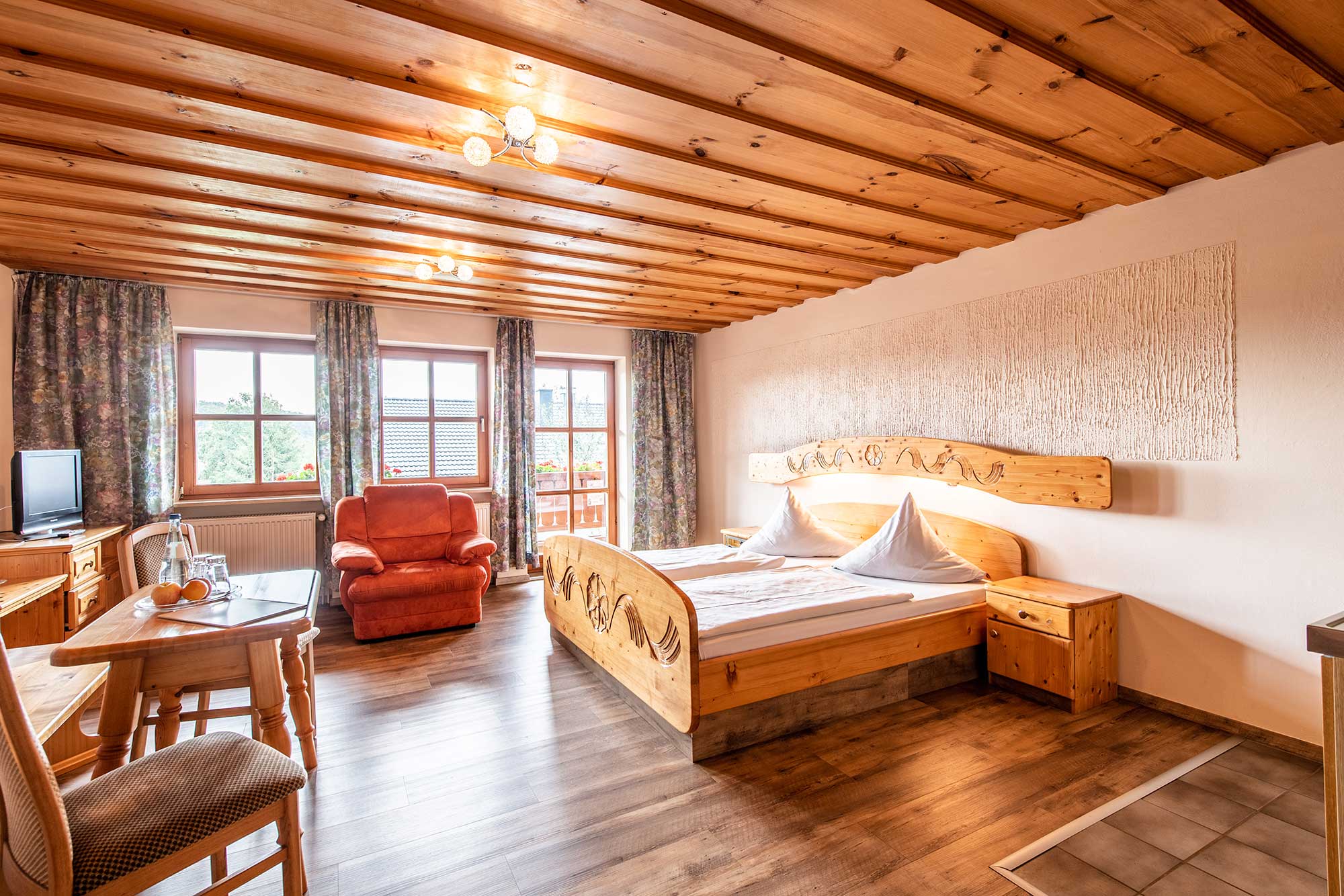 Eine Suite mit einem großen Doppelbett, einem roten Sessel und einem Fernseher im Hotel Der Böhmerwald
