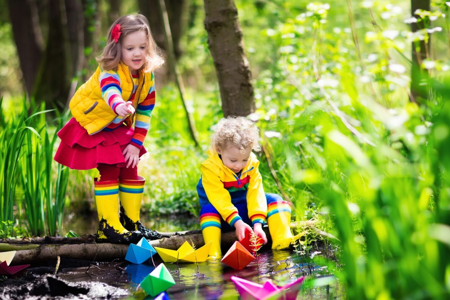 Bild der PauschaleF amilien Aktiv Tage mit einem Mädchen und Jungen in gelber Regenkleidung die mit Papierschiffen am Wasser spielen